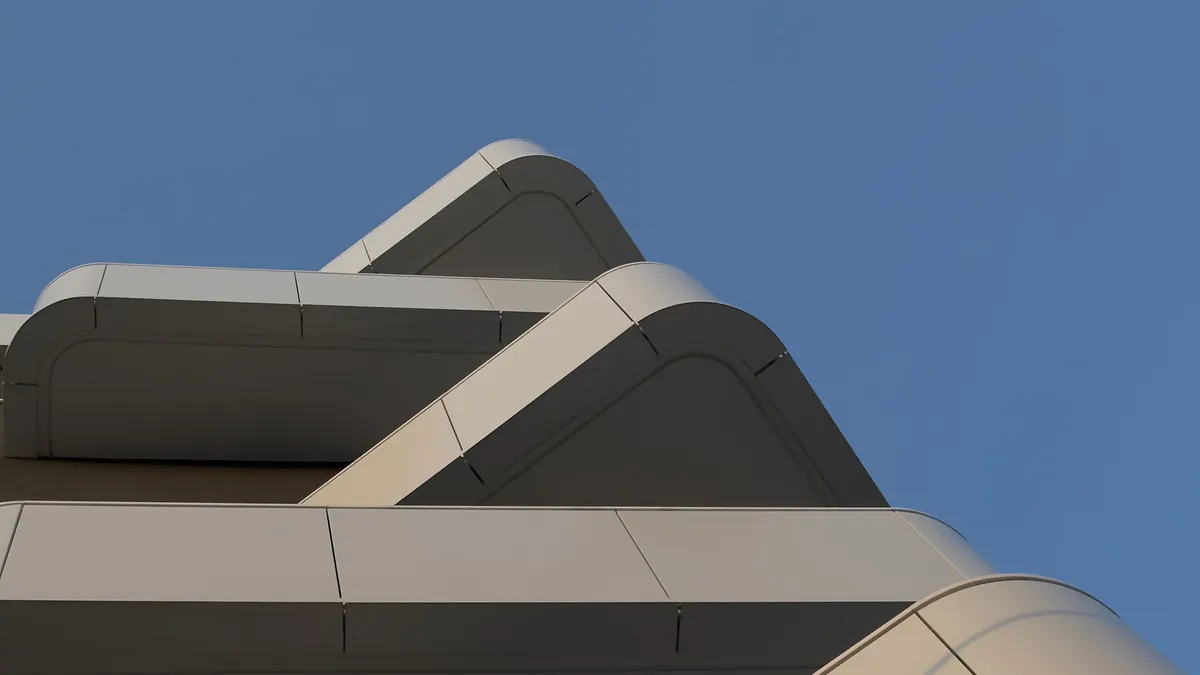 Pale, softly rounded concrete balconies of a modernist building, seen from below against a clear blue sky.